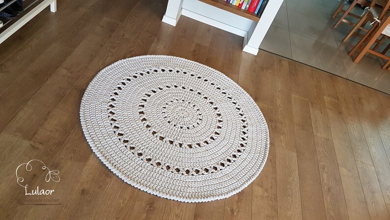 May include: A white crocheted round rug with a circular pattern. The rug is on a wooden floor.