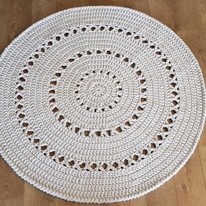 May include: A white crocheted round rug with a spiral pattern and openwork design.