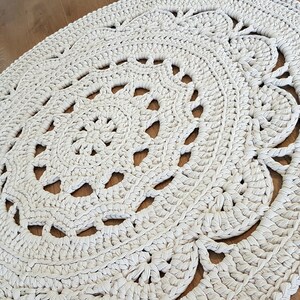 May include: A white crocheted rug with a circular design. The rug has a delicate, lacy pattern and is made with thick yarn.