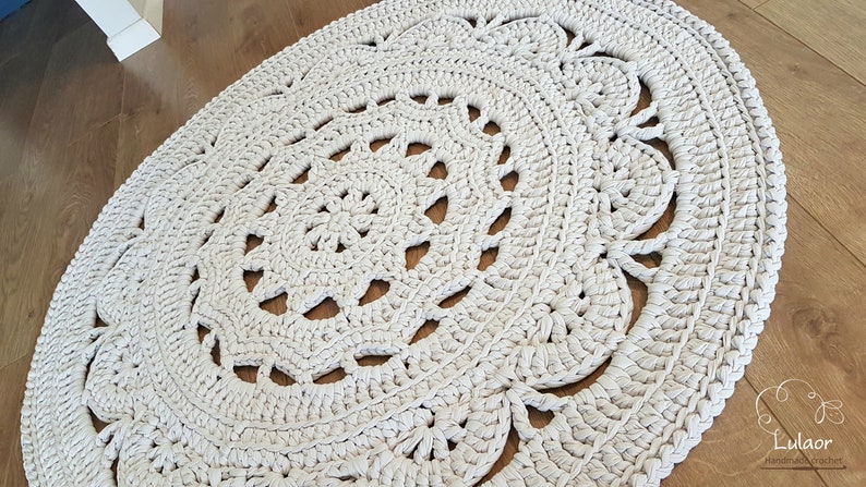 May include: A white crocheted rug with a circular design. The rug has a delicate, lacy pattern and is made with thick yarn.