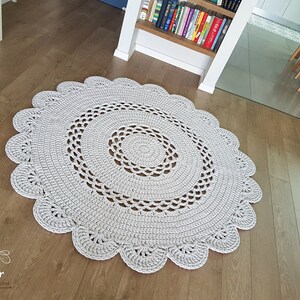 May include: A light gray, round, crocheted rug with a scalloped edge. The rug features a spiral design in the center and is made of a soft, textured yarn. The rug is approximately 47 inches in diameter, perfect for a living room or bedroom.