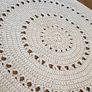 May include: A white crocheted round rug with a circular pattern of holes. The rug is made with thick yarn and has a textured surface.