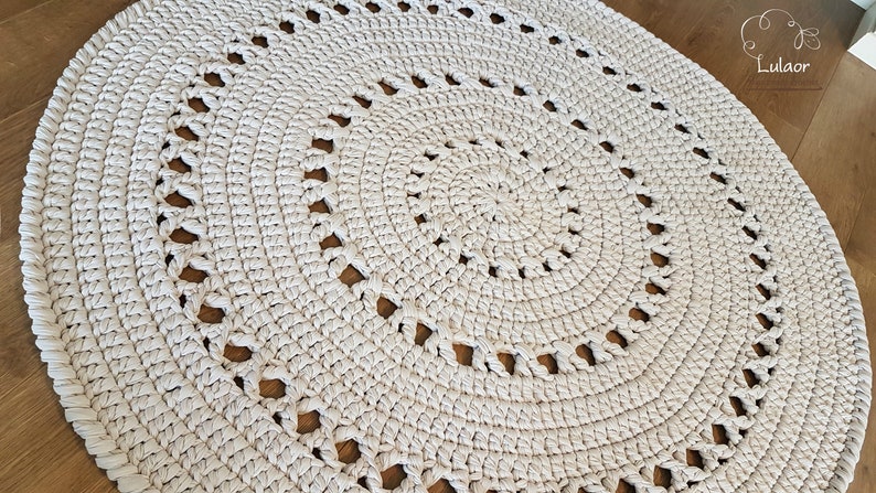 May include: A white crocheted round rug with a circular pattern of holes. The rug is made with thick yarn and has a textured surface.