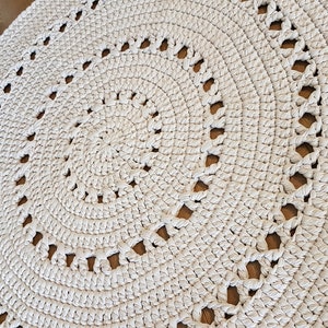 May include: A white crocheted round rug with a circular pattern of holes. The rug is made with thick yarn and has a textured surface.