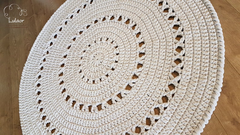 May include: A white crocheted round rug with a circular pattern of holes. The rug is made with thick yarn and has a textured surface.