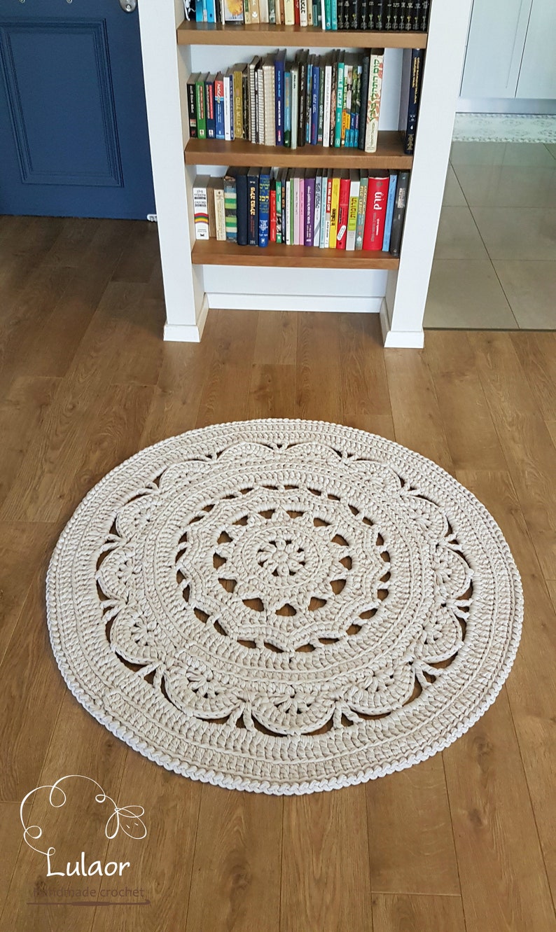 May include: A large, round, crocheted rug in a cream colour with a detailed, intricate design. The rug is made with thick yarn and has a delicate, lacy pattern.