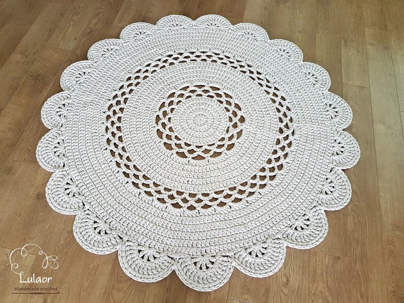 May include: A round, off-white crochet rug with a scalloped edge. The rug features concentric circles of openwork and solid crochet stitches. The rug is approximately 47 inches in diameter, suitable for a living room or bedroom.