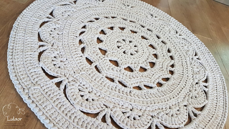 May include: A white crocheted round rug with a delicate floral pattern. The rug has a circular design with intricate details and a soft, textured surface.