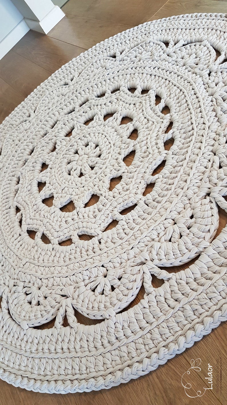 May include: A large, round, crocheted rug in a cream colour with a delicate, lacy pattern. The rug is made with thick yarn and has a soft, textured surface.