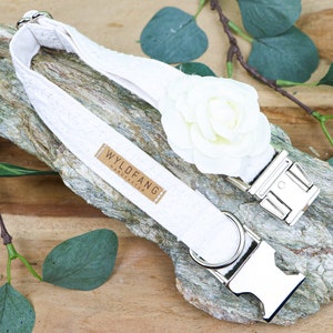May include: White cotton dog collar with a white fabric flower and silver metal buckle. The collar has a brown leather tag with the text "WYLD FANG HANDMADE".