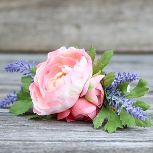 May include: A pink and white ranunculus flower with purple lavender sprigs and green leaves.