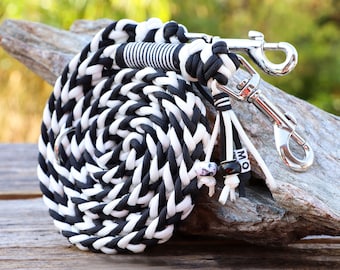 May include: Black and white braided dog leash with a silver clip and beads. The leash is coiled on a piece of driftwood.