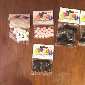 May include: Five packages of craft supplies, each containing a different color of pom poms or black felt shapes. The packages are labeled "Carnival of Crafts".