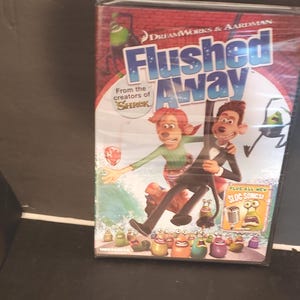 May include: A DVD of the animated film "Flushed Away" featuring characters from the movie. The cover art shows two main characters, a male and female, with the title in large, colorful letters. The DVD is sealed in plastic.