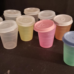 May include: A collection of small, colorful plastic cups with matching lids. The cups are in various colors, including clear, yellow, pink, orange, and blue. The lids are white or match the cup color. These cups are likely for portion control or small servings.