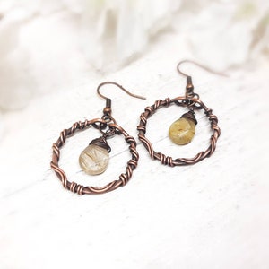 May include: A pair of copper wire earrings with a teardrop-shaped, light brown gemstone hanging from each hoop.