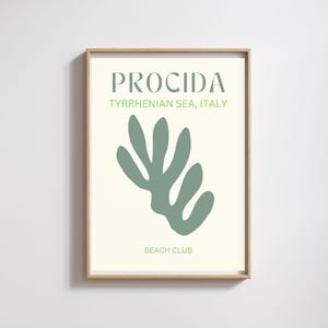 May include: A framed art print featuring the word "PROCIDA" in a light green font, with "TYRRHENIAN SEA, ITALY" below it. A light green abstract shape is in the center, with "BEACH CLUB" at the bottom.