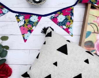 May include: A white throw pillow with black triangle designs. The pillow is on a white wooden surface with a floral fabric garland hanging above it.