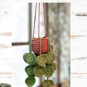 May include: A crochet hanging plant holder with heart-shaped leaves. The plant holder is a mix of orange and green, with a matching cord for hanging. The text "PDF CROCHET PATTERN Heart-Leaf Hanging Plant" is at the top, and "Topaz Eyez Crochet" is at the bottom.