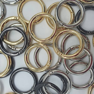 Könnte beinhalten: Eine Sammlung verschiedener Schlüsselringe aus Metall in Gold-, Silber- und Schwarz-Finish. Die Schlüsselringe sind in verschiedenen Größen und Formen erhältlich, einige haben einen Drehverschluss.