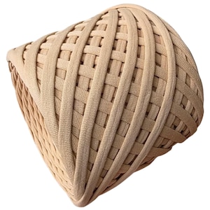 Könnte beinhalten: Ein geflochtenes Haarband in hellem Beige. Das Haaraccessoire hat ein Korbgeflechtmuster, bei dem sich vertikale und horizontale Bänder kreuzen und eine strukturierte Oberfläche bilden. Das Material wirkt weich und flexibel, geeignet für Frisuren.