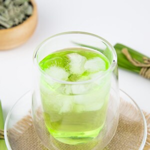 May include: A glass of green iced tea with ice cubes in a double-walled glass. The glass is sitting on a brown woven placemat.