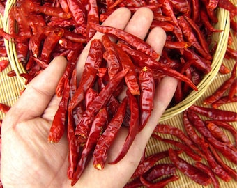 May include: A hand holding a pile of dried red chili peppers. The peppers are long and thin, and they are arranged in a pile in the palm of the hand.