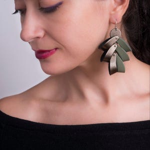 Puede incluir: Un par de pendientes de cuero verde y plateado con un diseño geométrico. Los pendientes son colgantes y tienen un aspecto en capas.