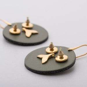 May include: A pair of green leather earrings with gold fishtail charms. The earrings are circular and have a hook closure.