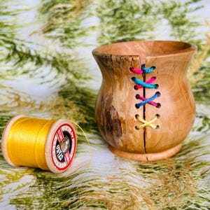 May include: A wooden bowl with a unique design featuring colorful threads woven through the wood. The bowl is sitting on a green and brown patterned fabric.