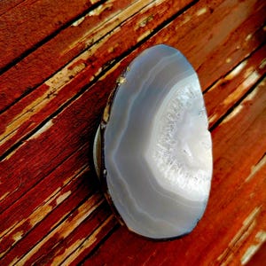 May include: A gray and white agate slice with a natural, organic shape. The slice has a smooth, polished surface and a white center with gray bands radiating outward.