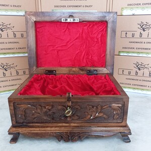 May include: An open wooden box with a red velvet lining. The box has intricate carvings on the front and sides. The box is labeled "tubibu" and "Handmade & Original".