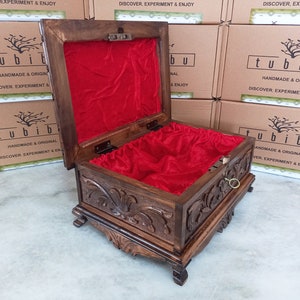 May include: A wooden box with intricate carvings and a red velvet interior. The box is open and the lid is propped up. The box has a brass handle and is sitting on a white surface. The box has the text "tubibu" on the front and the words "Handmade & Original" and "Discover, Experiment & Enjoy" on the side.