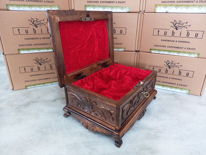 May include: A wooden box with intricate carvings and a red velvet interior. The box is open and the lid is propped up. The box has a brass handle and is sitting on a white surface. The box has the text "tubibu" on the front and the words "Handmade & Original" and "Discover, Experiment & Enjoy" on the side.