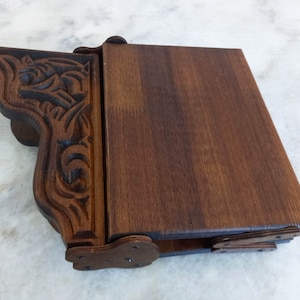 May include: A dark brown wooden box with a carved decorative side. The box has a hinged lid and is made of stained wood. The carved side features an ornate design. The box is likely used for storage or display.