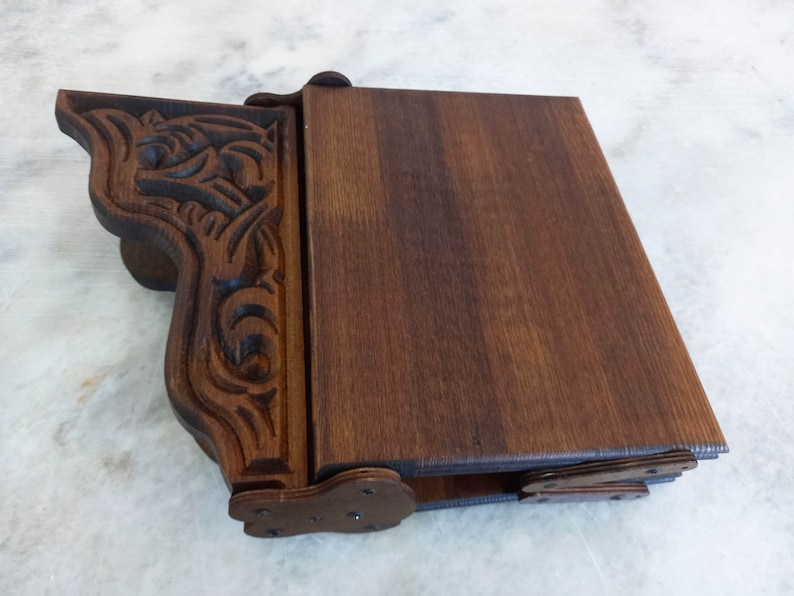 May include: A dark brown wooden box with a carved decorative side. The box has a hinged lid and is made of stained wood. The carved side features an ornate design. The box is likely used for storage or display.