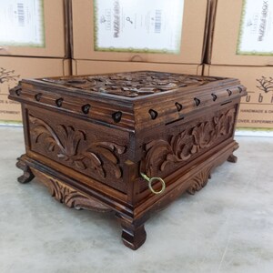 May include: A wooden puzzle box with intricate carvings and a keyhole. The box is dark brown and has a decorative design on the top and sides. The box is sitting on a light brown surface.