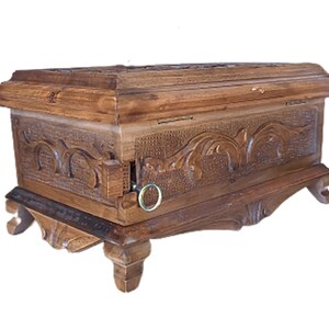May include: A wooden box with intricate carvings and a hinged lid. The box has a decorative metal ring on the side and sits on four carved legs.