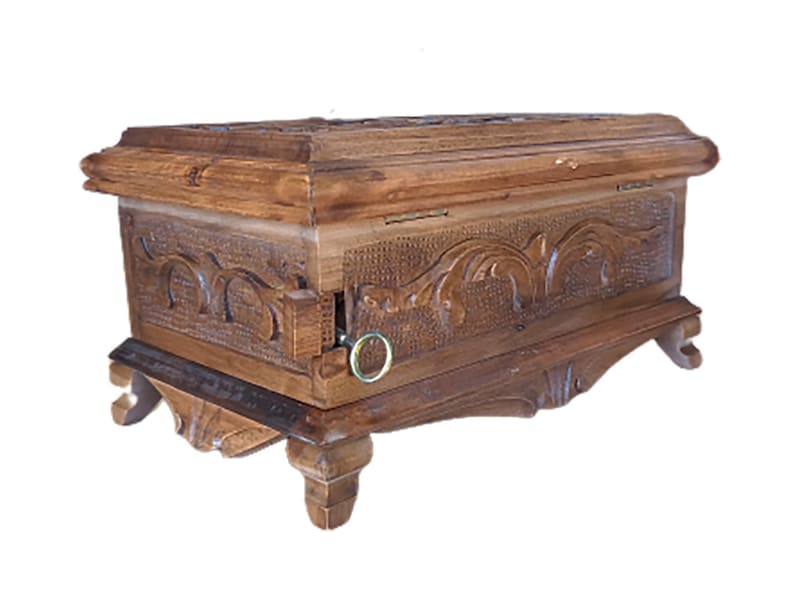 May include: A wooden box with intricate carvings and a hinged lid. The box has a decorative metal ring on the side and sits on four carved legs.