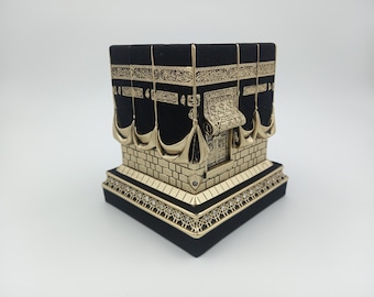 Pode incluir: Um modelo preto e dourado da Caaba, um edifício em forma de cubo em Meca, Arábia Saudita, que é o santuário mais sagrado do Islã. O modelo é feito de madeira e metal e é decorado com detalhes intrincados.
