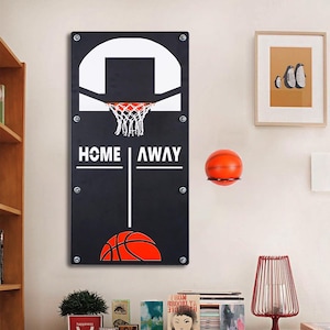May include: A black basketball hoop wall decor with a white backboard, net, and the words "HOME | AWAY". An orange basketball sits on a small shelf. A framed picture of penguins hangs on the wall.