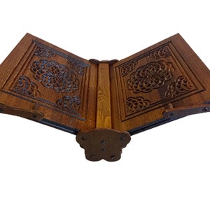 May include: A wooden book stand with intricate floral carvings. The stand is made of dark brown wood and features a hinged design for adjustable positioning. The carvings are detailed and add a decorative element to the stand.