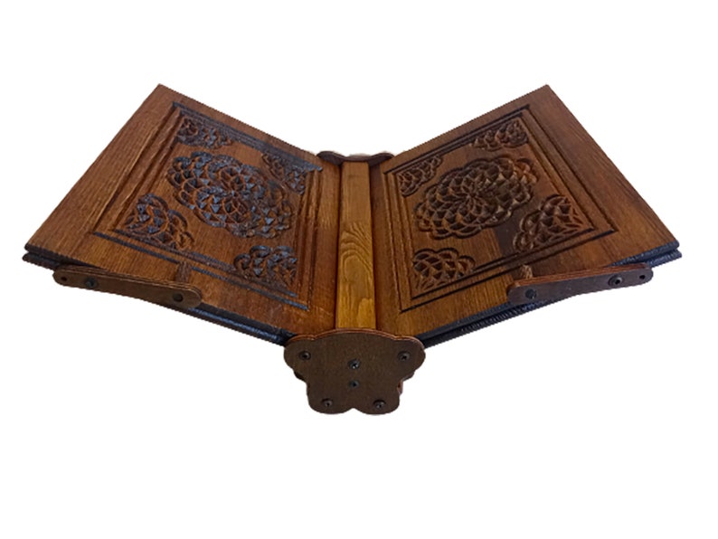 May include: A wooden book stand with intricate floral carvings. The stand is made of dark brown wood and features a hinged design for adjustable positioning. The carvings are detailed and add a decorative element to the stand.
