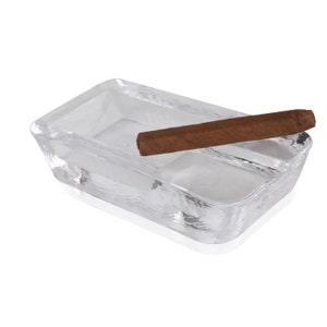 May include: A clear glass rectangular ashtray with a brown cigar resting on the edge.