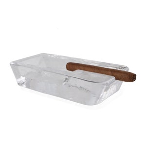May include: A clear glass rectangular ashtray with a brown cigar resting on the edge.
