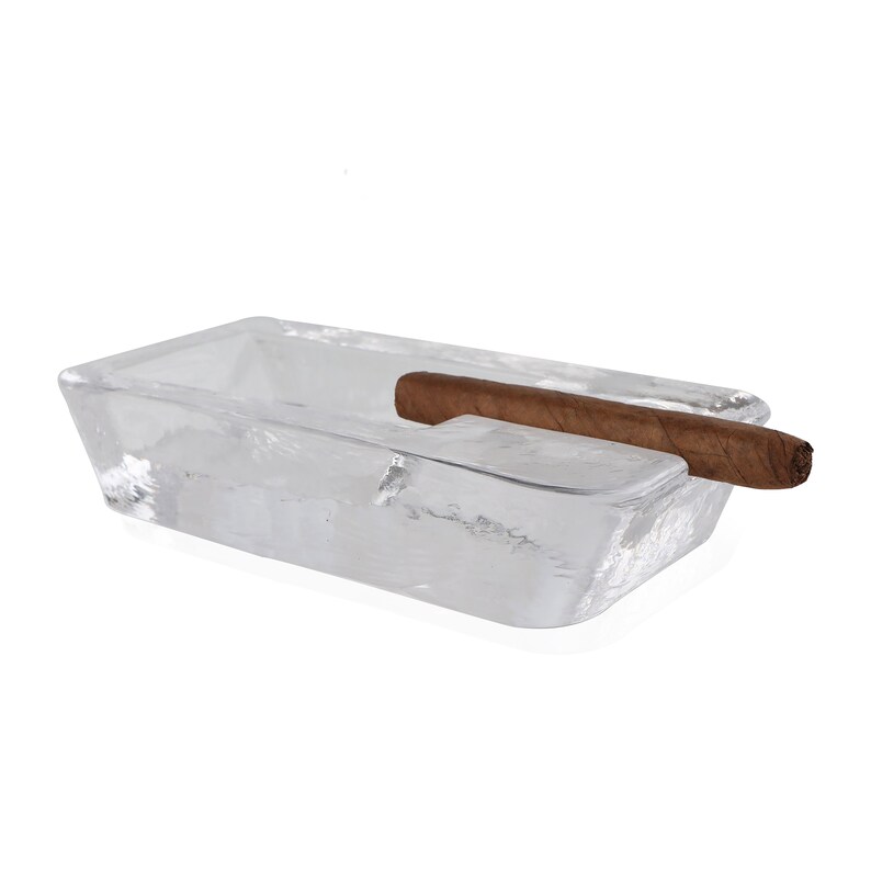 May include: A clear glass rectangular ashtray with a brown cigar resting on the edge.