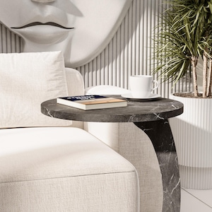 Puede incluir: Un sof&aacute; blanco con un coj&iacute;n blanco y una mesa auxiliar de m&aacute;rmol negro con un libro titulado "Strength of a Woman" encima. Una taza y un platillo blancos est&aacute;n sobre la mesa.