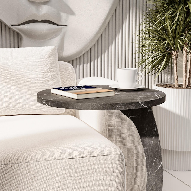 Puede incluir: Un sof&aacute; blanco con un coj&iacute;n blanco y una mesa auxiliar de m&aacute;rmol negro con un libro titulado "Strength of a Woman" encima. Una taza y un platillo blancos est&aacute;n sobre la mesa.