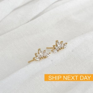 May include: A pair of gold earrings with a delicate, curved design featuring a row of clear, marquise-shaped stones.