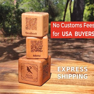 May include: Three wooden cubes stacked on top of each other. Each cube has a QR code and text. The top cube says "Facebook", the middle cube says "Menu", and the bottom cube has a raven illustration and says "Rellik Winery".